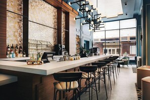 A modern bar area with a long counter, bar stools, and a patterned wall. - Kinley Cincinnati Downtown, a Tribute Portfolio Hotel (Cincinnati)