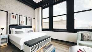 A modern hotel room with a large bed, a side table, a sofa, and a view of the cityscape through large windows. - Kinley Cincinnati Downtown, a Tribute Portfolio Hotel (Cincinnati)