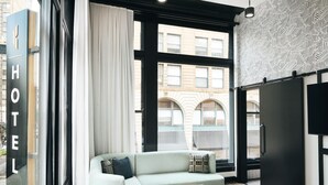 A modern hotel room with a large window, a sofa, a small round table, and a wardrobe. - Kinley Cincinnati Downtown, a Tribute Portfolio Hotel (Cincinnati)
