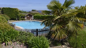 Piscina cercada por vegetação exuberante e um cercado de madeira.