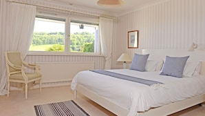 Quarto com uma cama grande, uma cadeira, uma janela com cortinas e um radiador.