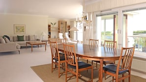 Uma sala de estar ampla, com espaço de jantar, um conjunto de sofás, um candelabro e vista através de grandes janelas.