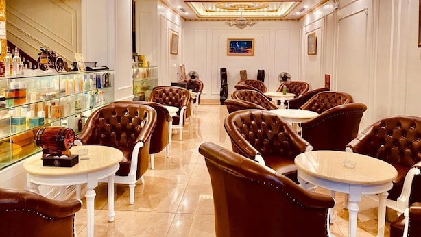 A luxurious hotel lobby with leather chairs, a bar area, and a chandelier.