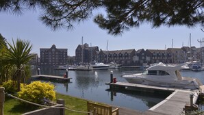 Un puerto deportivo con barcos amarrados, un muelle de madera y una hilera de edificios residenciales al fondo.