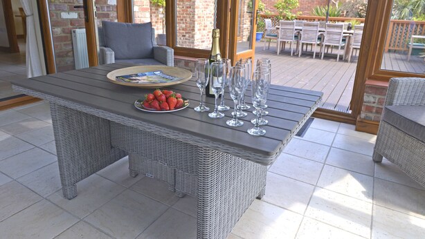 Un patio cubierto con una mesa de mimbre, un plato de fresas, copas de vino y una botella de champán.