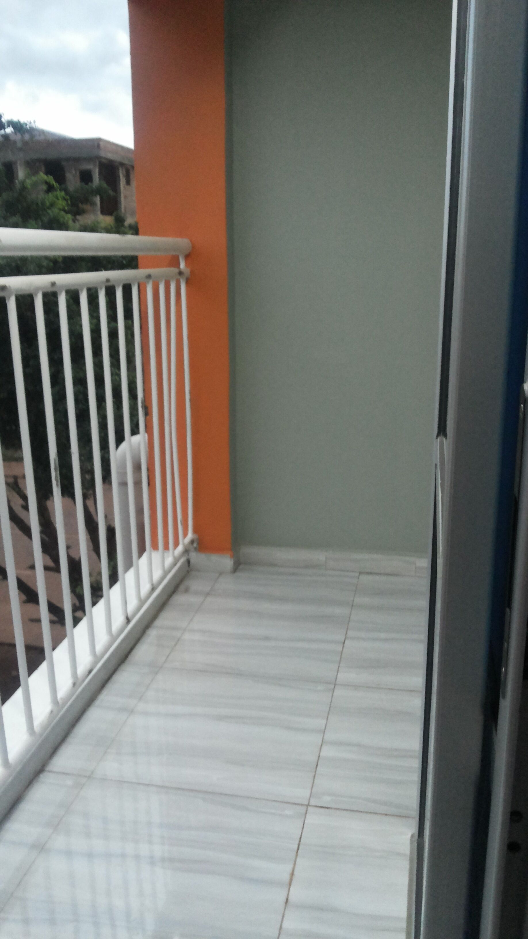 Un balcón con barandillas blancas, una pared gris y un piso de baldosas.