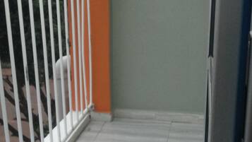Un balcón con barandillas blancas, una pared gris y un piso de baldosas.