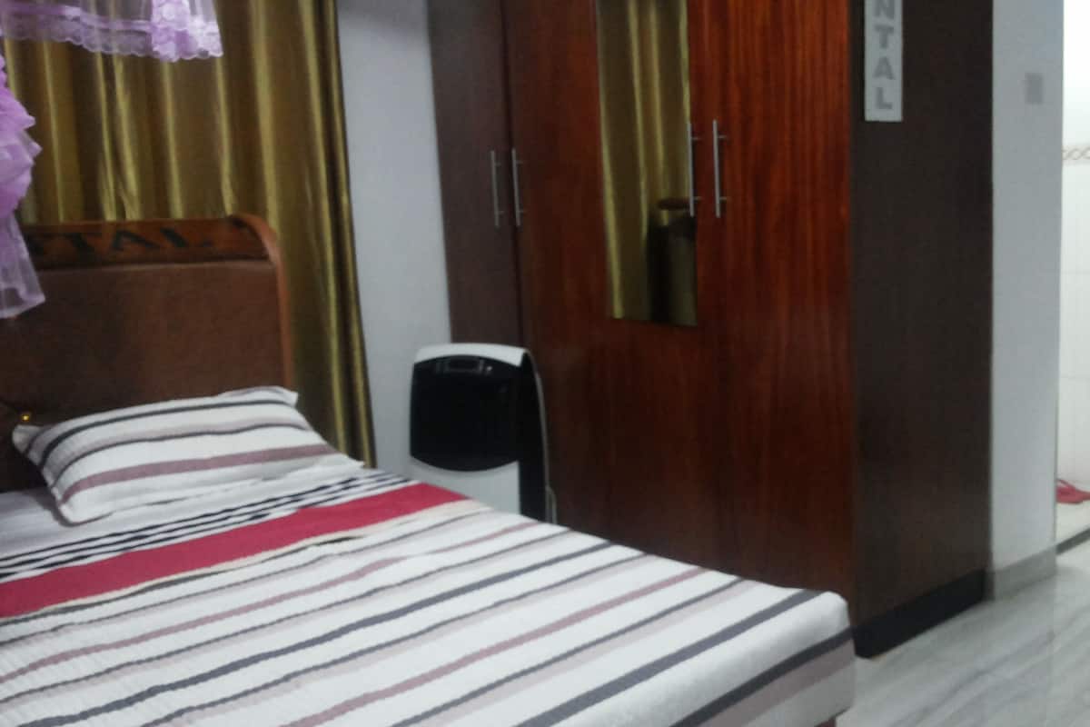 Une chambre d’hôtel comprenant un lit, une armoire en bois, une table de chevet et un téléphone fixé au mur.