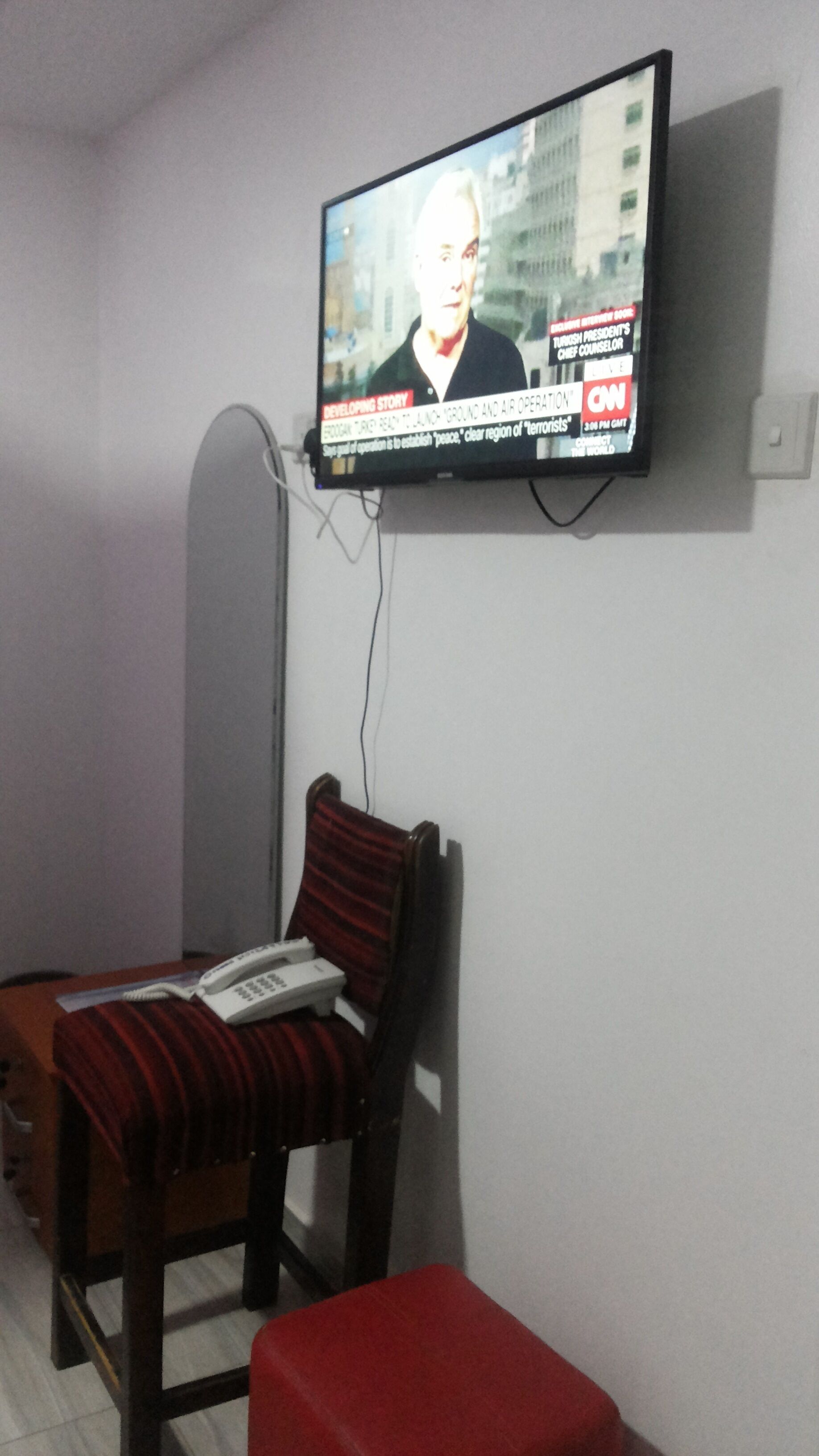 A television mounted on a wall displaying a news broadcast.
