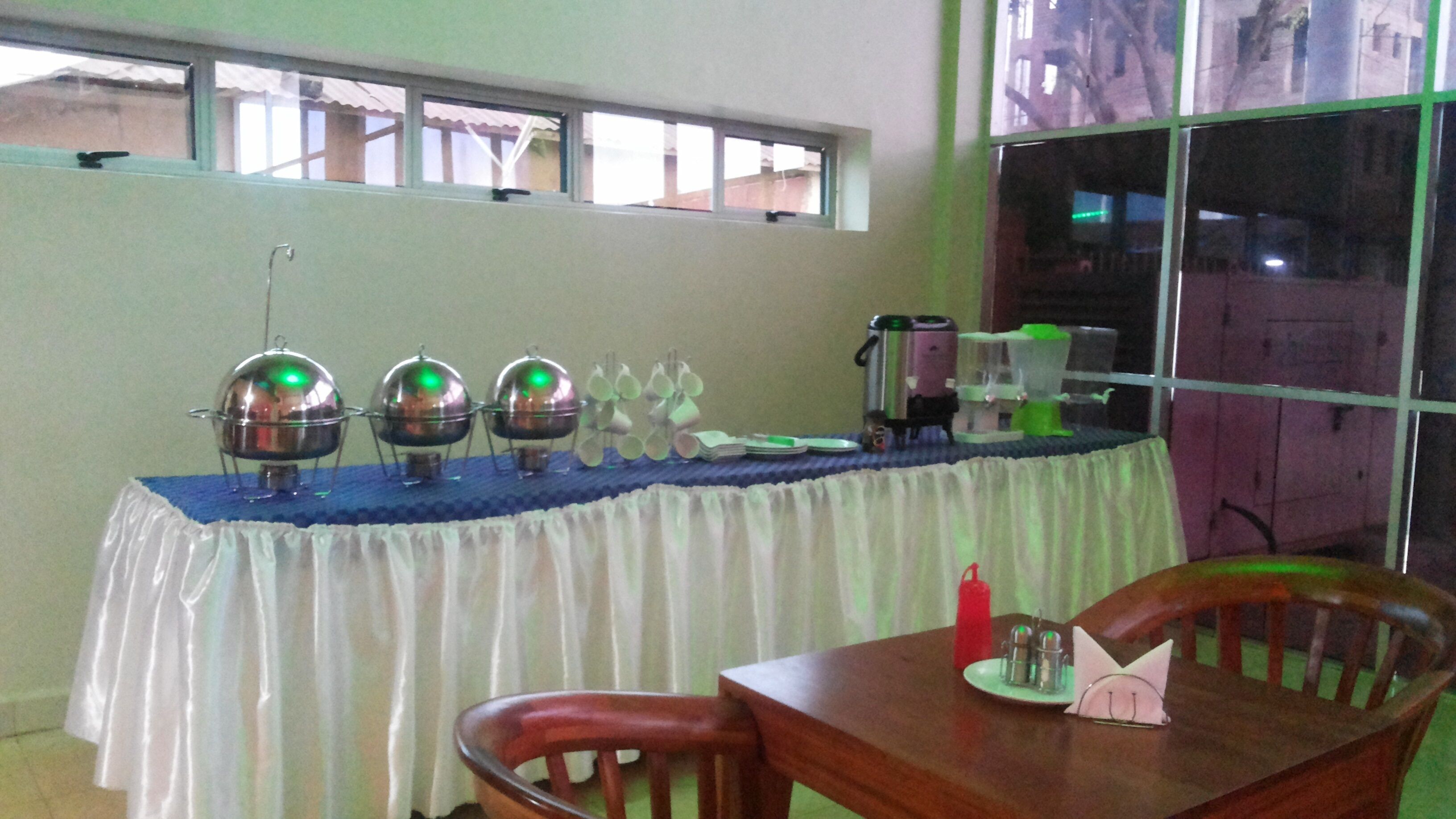 A dining area with a table set for four, a window with a view of buildings, and a table with a blue tablecloth and various items on it.