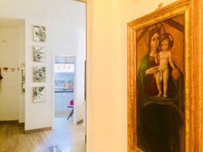 A hallway with a framed painting of a religious figure, a kitchen area, and several wall-mounted artworks.