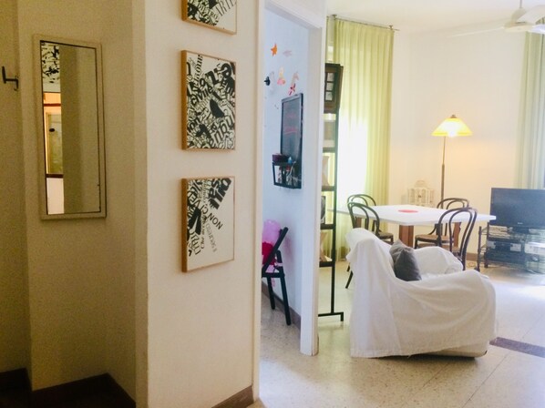 A living room with a sofa, a dining table, and a TV. There are wall decorations and a lamp.
