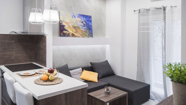 A modern living room with a sofa, a dining table with plates and a fruit bowl, a small wooden side table, and a painting on the wall. - InCity La Central 203, Deluxe Flat (Thessaloniki)