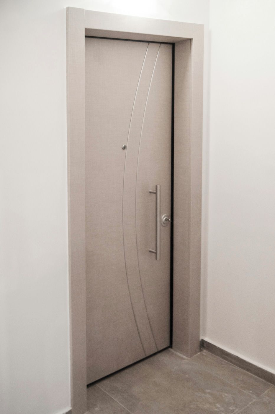 Puerta cerrada con picaporte y cerradura, ubicada en un rincón junto a una pared lisa y un piso de baldosas.