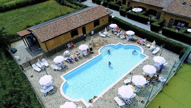 Una piscina con sillas de descanso y sombrillas, rodeada por una terraza de piedra y adyacente a un edificio con techo de tejas.