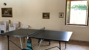 Una mesa de ping pong en una habitación con suelo de baldosas, techo de madera y ventana con vistas al verdor.