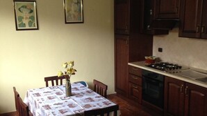 Un comedor con una mesa dispuesta para cuatro personas, rodeada de sillas de madera. Hay un florero con flores sobre la mesa. La habitación tiene armarios de madera y piso de baldosas.
