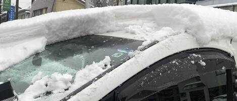 Un coche cubierto de nieve, con un cartel de "Snow House Memorie" al fondo.