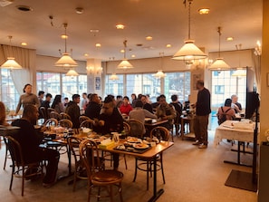 A restaurant with multiple tables and chairs, large windows, and hanging lamps. - SnowHouse Memorie (Minamiuonuma)