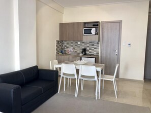 A compact living space with a kitchenette, a dining area with a table and chairs, and a black sofa. - InCity El Metro 102, Deluxe Studio (Thessaloniki)