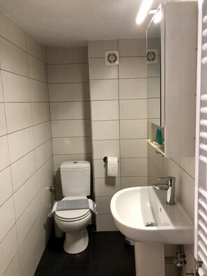 A small, modern bathroom with white tiles, a toilet, a sink, and a mirror. - InCity El Metro 102, Deluxe Studio (Thessaloniki)