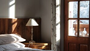 Une chambre à coucher avec une tête de lit en bois, une table de chevet avec une lampe, une fenêtre avec des rideaux et un lit avec des oreillers.