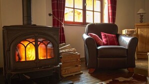 Une pièce chaleureuse avec un poêle à bois, un fauteuil en cuir agrémenté de coussins rouges et un plancher en bois rustique.