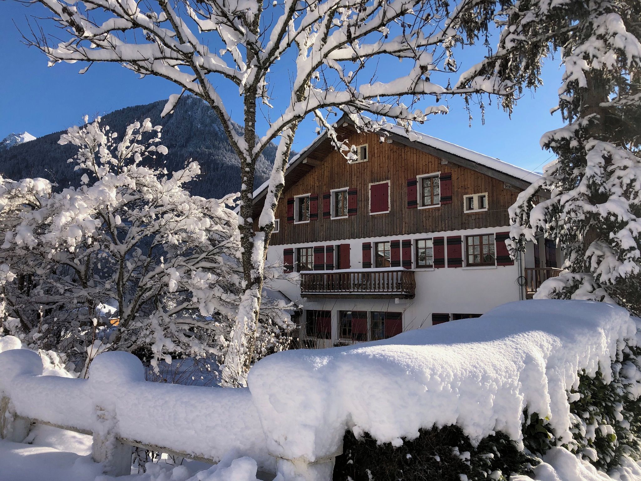 Un chalet en bois doté d’un balcon, entouré d’arbres couverts de neige et avec des montagnes en toile de fond.