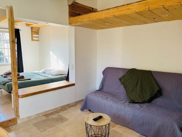 Una habitación con cama, sofá, una pequeña mesa redonda y una silla colgante.