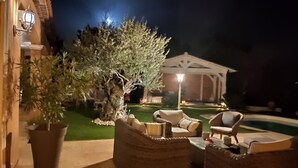 An outdoor seating area with wicker furniture and a well-lit building in the background. - House in the heart of green Provence and 35 minutes from the beaches (Gareoult)