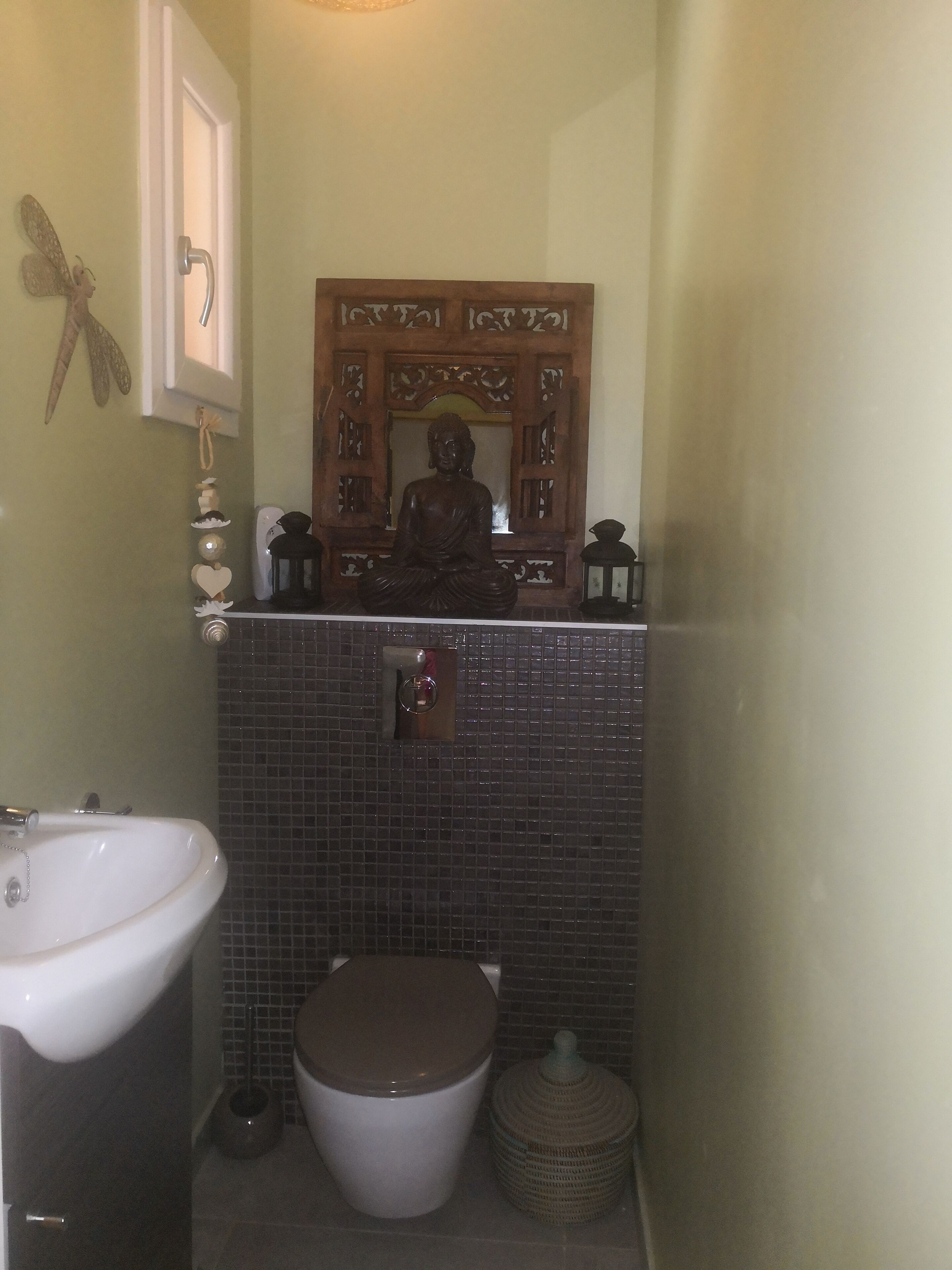 Un baño con inodoro, lavamanos y una estatua decorativa de Buda sobre el espejo.