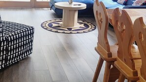 Ein geräumiges Wohnzimmer mit einem blauen Sofagarnitur, einem Holzespeisetisch mit Stühlen und großen Fenstern mit Blick auf den Garten.