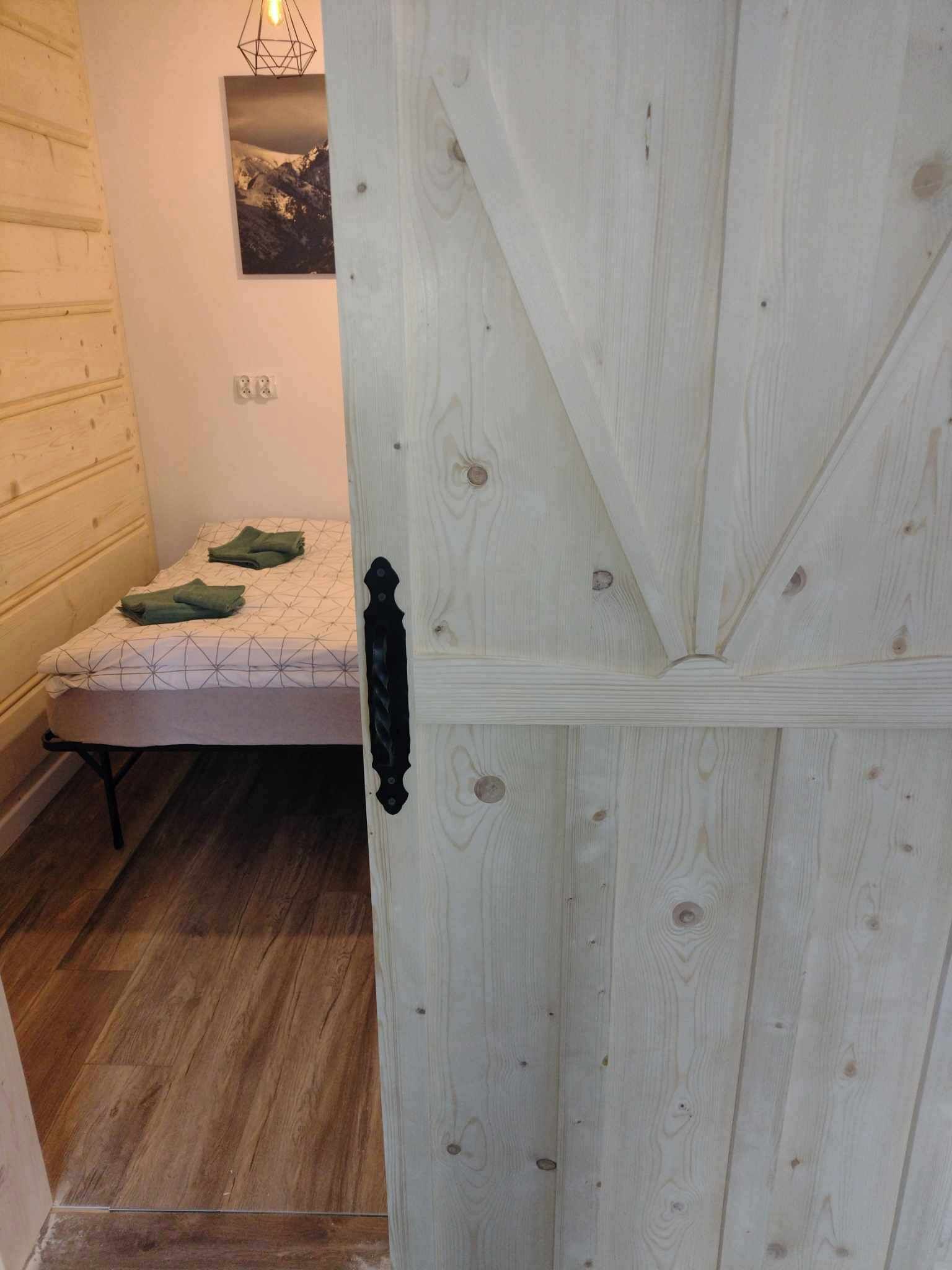 Huone, jossa on sänky, puinen ovi ja seinälle ripustettu taulu.