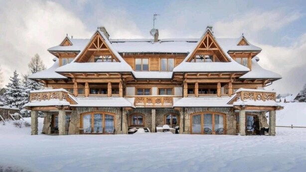 Eine große, mehrstöckige Holzlodge mit symmetrischer Gestaltung, einem zentralen Eingang und mehreren Balkonen.