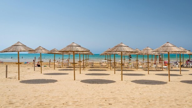 A beach with thatched umbrellas and sun loungers, a clear blue sky, and the ocean in the background. - Sicily Bedda vacation home, apartment in the city center and a stone's throw from the sea! (Pozzallo)
