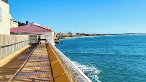A coastal promenade with a wooden walkway, a building with a red roof, and a clear view of the sea. - Sicily Bedda vacation home, apartment in the city center and a stone's throw from the sea! (Pozzallo)