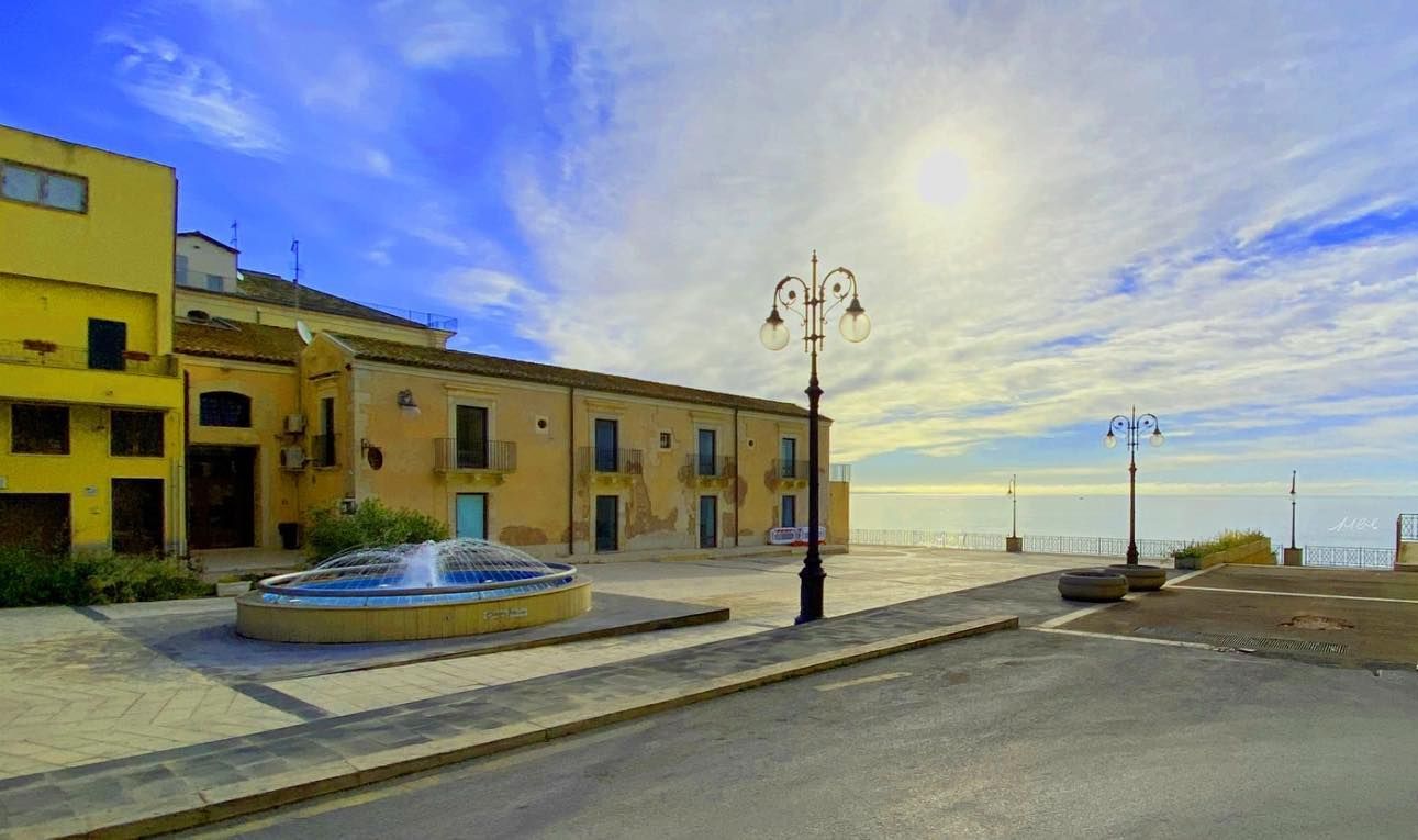 Une place publique avec une fontaine, un lampadaire et des bâtiments de part et d’autre.