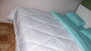 A bed with a white quilt and teal pillows in a room with a tiled floor.