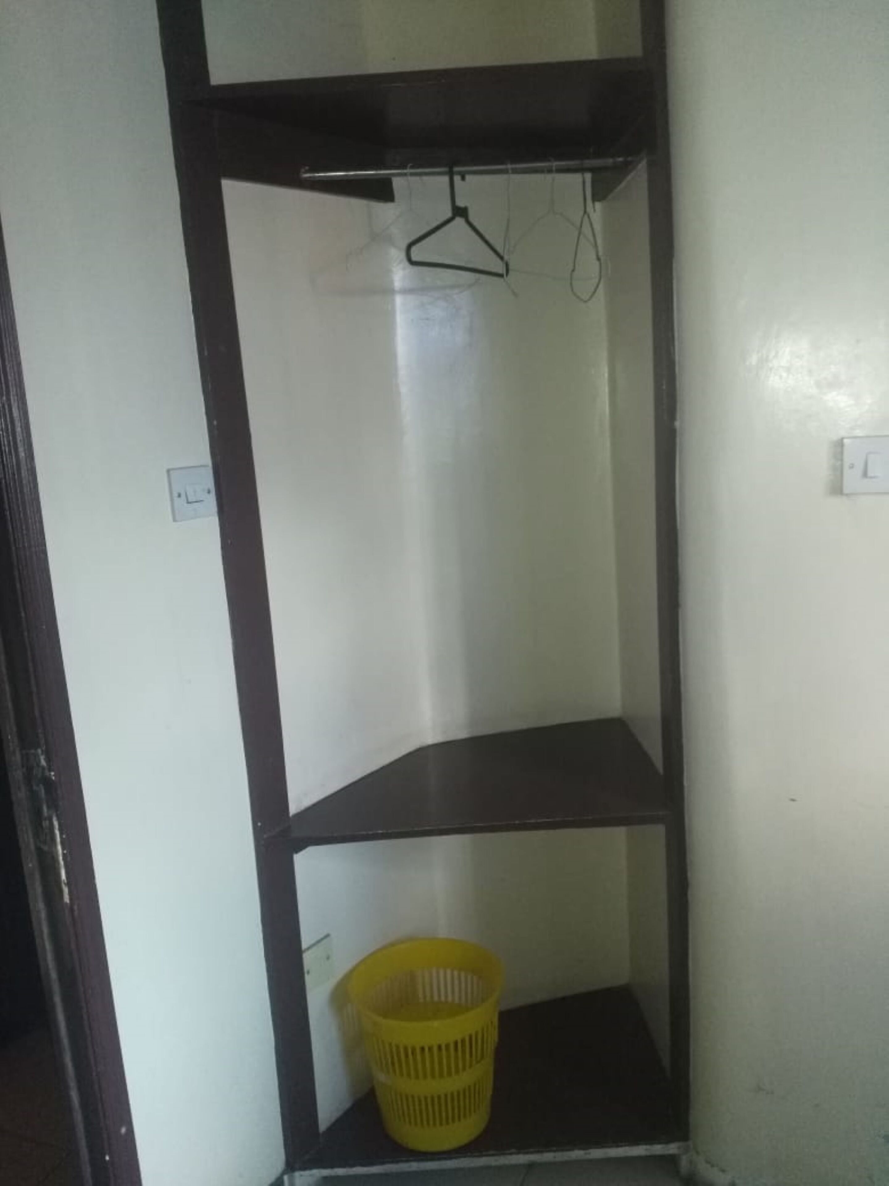 A room with a single yellow basket on the lower shelf and a black hanger on the upper shelf.