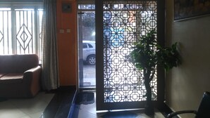 A reception area with a patterned partition, a sofa, a potted plant, and a door leading outside.