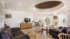 A spacious living room with a fireplace, leather sofas, a television, and a dining area. - Lila - Stunning sea views from this villa with infinity pool (Sesmarias)