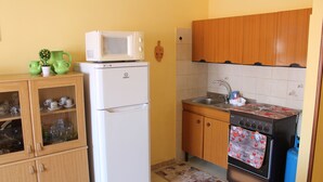 Een kleine keuken met een witte koelkast, een magnetron, een fornuis en houten kastjes.
