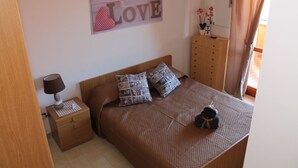 Een slaapkamer met een bed, nachtkastje, dressoir en een decoratie aan de muur.