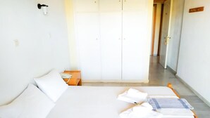 A bedroom with a bed, two pillows, a nightstand, a wardrobe, and a bathroom door. - Zagamilos Hotel (Pylos-Nestoras)