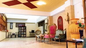 A spacious lobby with a high ceiling, a large bookshelf, and ornate furniture including a red upholstered chair and a green velvet armchair. - Zagamilos Hotel (Pylos-Nestoras)