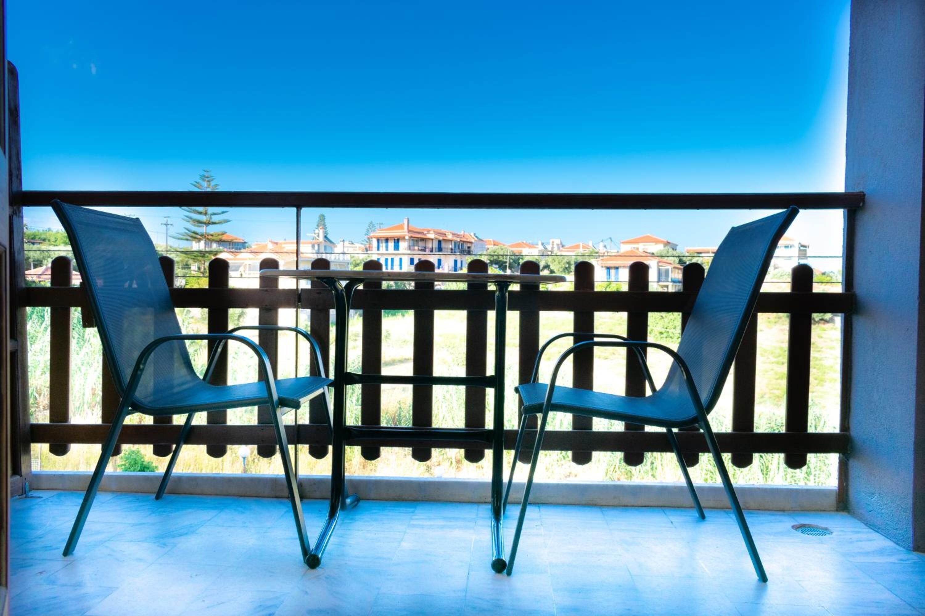 A balcony with two chairs and a table, overlooking a residential area with houses.