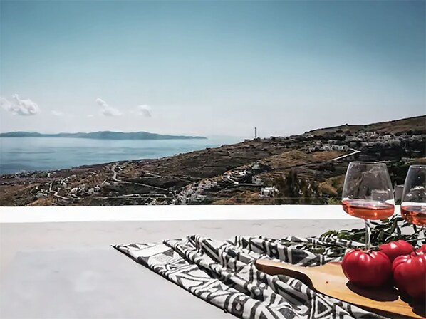 A table with a patterned tablecloth, two wine glasses with red wine, and a wooden board with red apples.