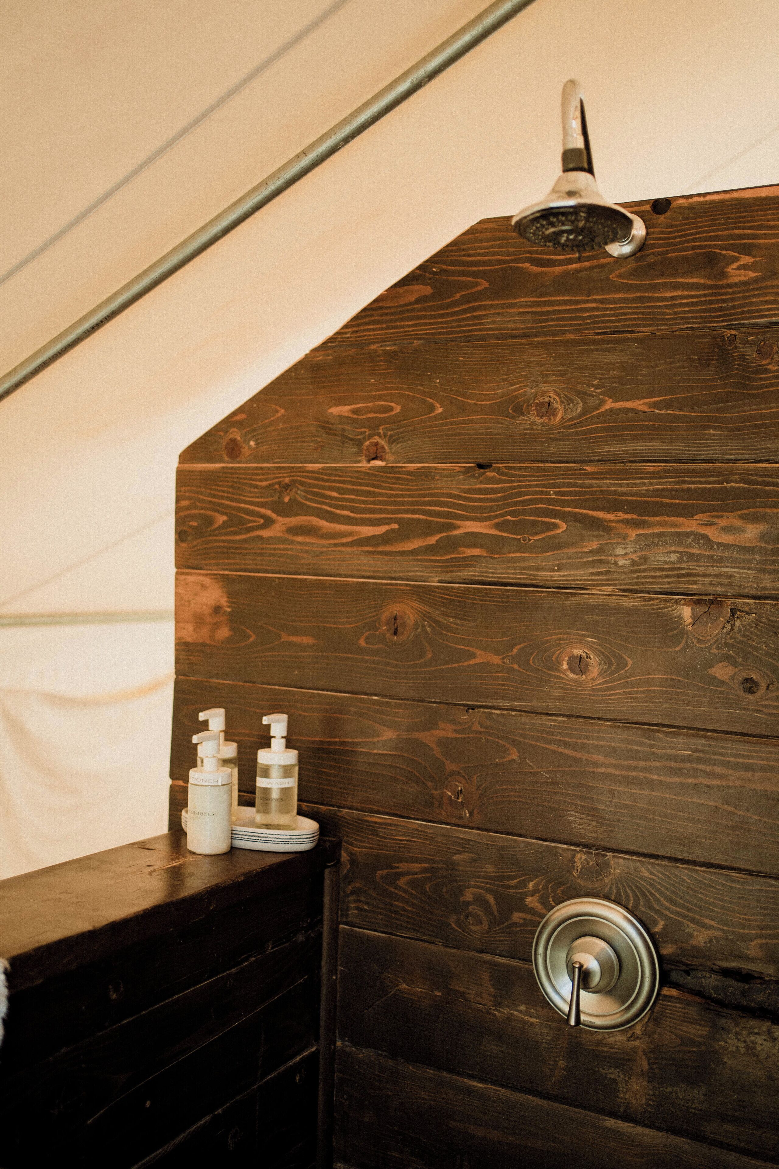 Pared de madera con cabezal de ducha, perchero y dispensador de jabón.