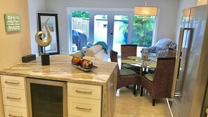 A kitchen with a marble countertop, a refrigerator, and a dining area with wicker chairs and a table.