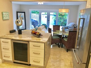 Una cocina con encimera de mármol, refrigerador y comedor con sillas de mimbre y una mesa.